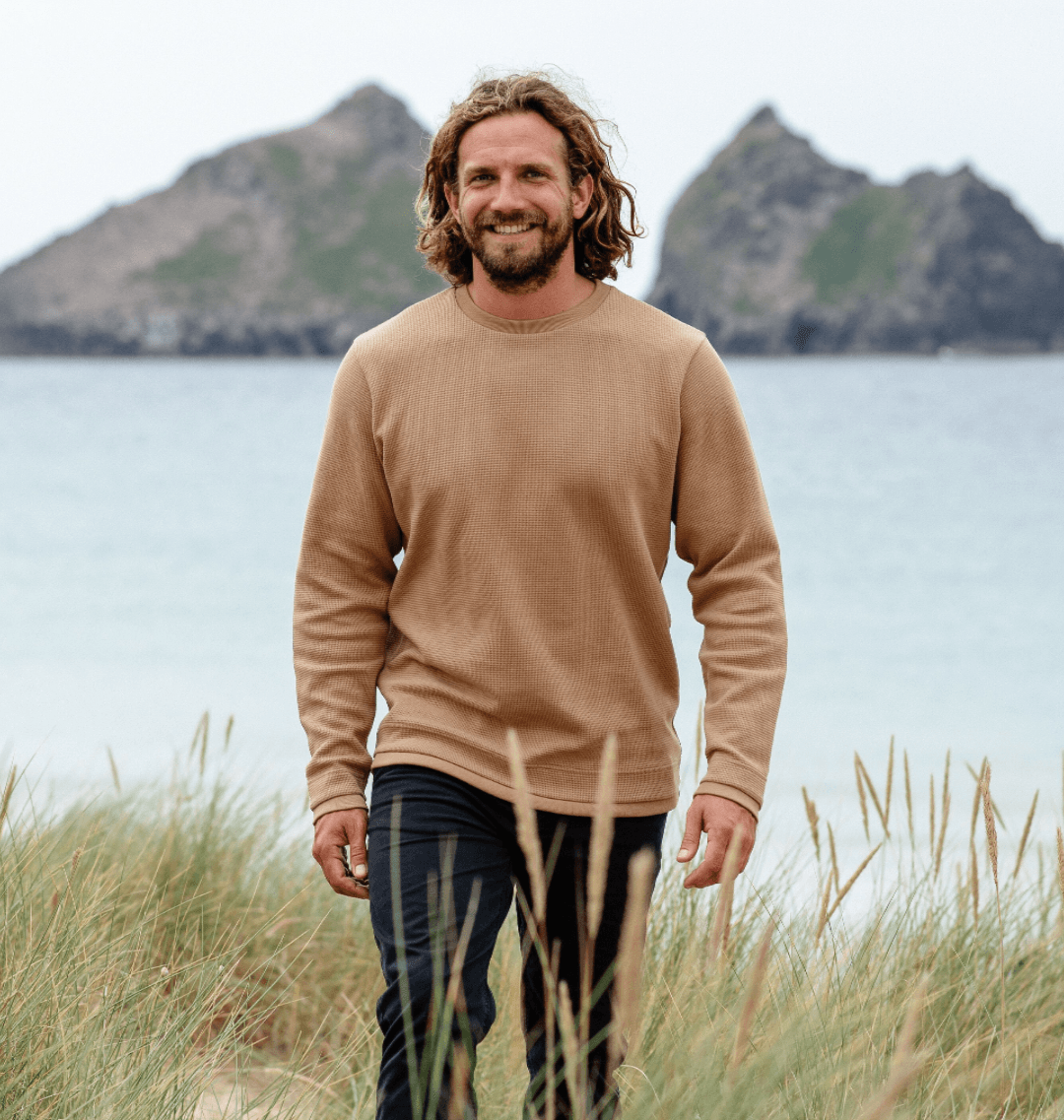 Man wearing men's waffle jumper in sand colour on a beach